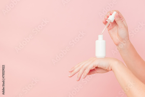 Hands holding glass bottle with dropper lid. White container with cosmetic product  serum  essential oil   on pink background. Concept of beauty