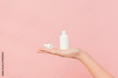 Hand holding glass bottle with dropper lid. White container with cosmetic product, serum (essential oil ) on pink background. Concept of beauty