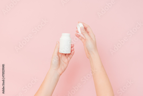 White bottle plastic tube in woman's hands on pink background. Packaging for pills, capsules or supplements. Cosmetics