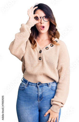 Beautiful young brunette woman wearing casual clothes and glasses doing ok gesture shocked with surprised face, eye looking through fingers. unbelieving expression.