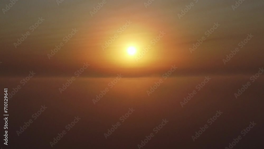 Toma aérea atravesando un mar de nubes en un amanecer con el sol en el centro del horizonte Toma aérea atravesando un mar de nubes en un amanecer con el sol en el centro del horizonte