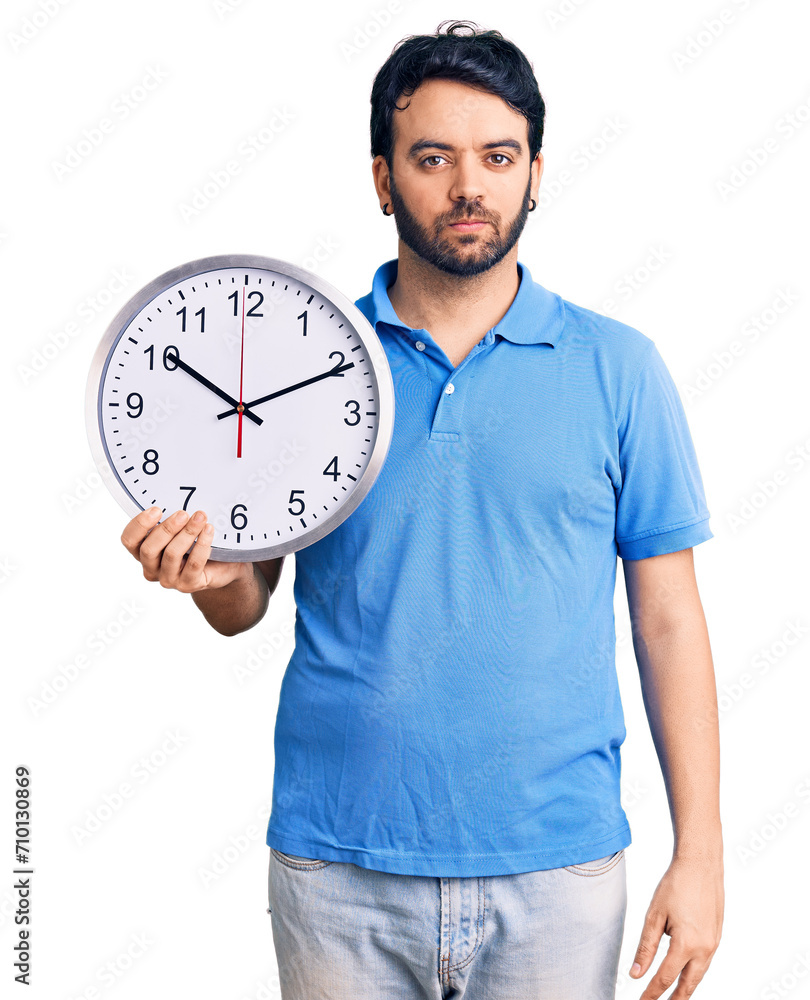 Young hispanic man holding big clock thinking attitude and sober expression looking self confident Young hispanic man holding big clock thinking attitude and sober expression looking self confident