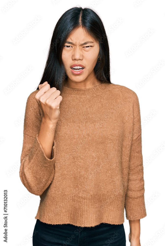 Beautiful young asian woman wearing casual winter sweater angry and mad raising fist frustrated and furious while shouting with anger. rage and aggressive concept. Beautiful young asian woman wearing casual winter sweater angry and mad raising fist frustrated and furious while shouting with anger. rage and aggressive concept.