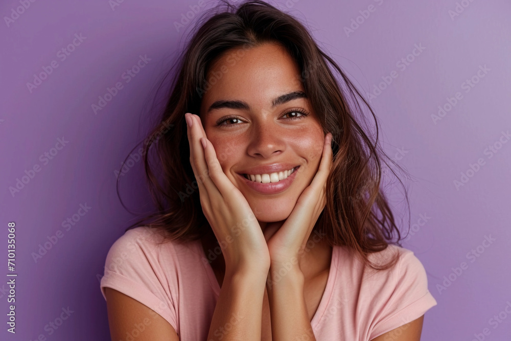 A charming serious Spanish-speaking brunette in a pink T-shirt on a purple background holds her hands near her face and smiles gently at the camera A charming serious Spanish-speaking brunette in a pink T-shirt on a purple background holds her hands near her face and smiles gently at the camera