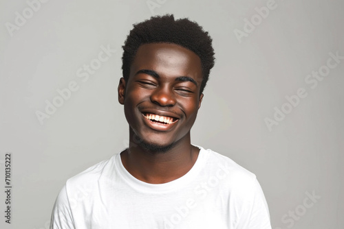 A handsome young African-American man in a white T-shirt is blinking his eyes with pleasure, wearing a happy expression. The concept of human facial expressions and emotions photo