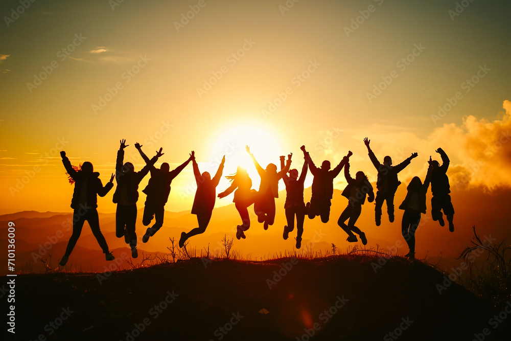 Silhouette of a group of people jumping in the air against the background of a bright sunrise in the mountains