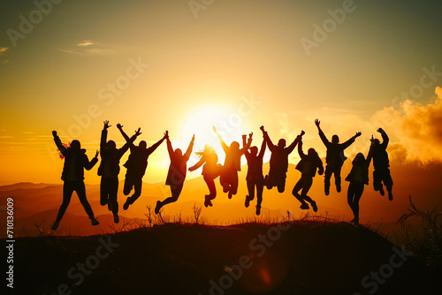 Silhouette of a group of people jumping in the air against the background of a bright sunrise in the mountains