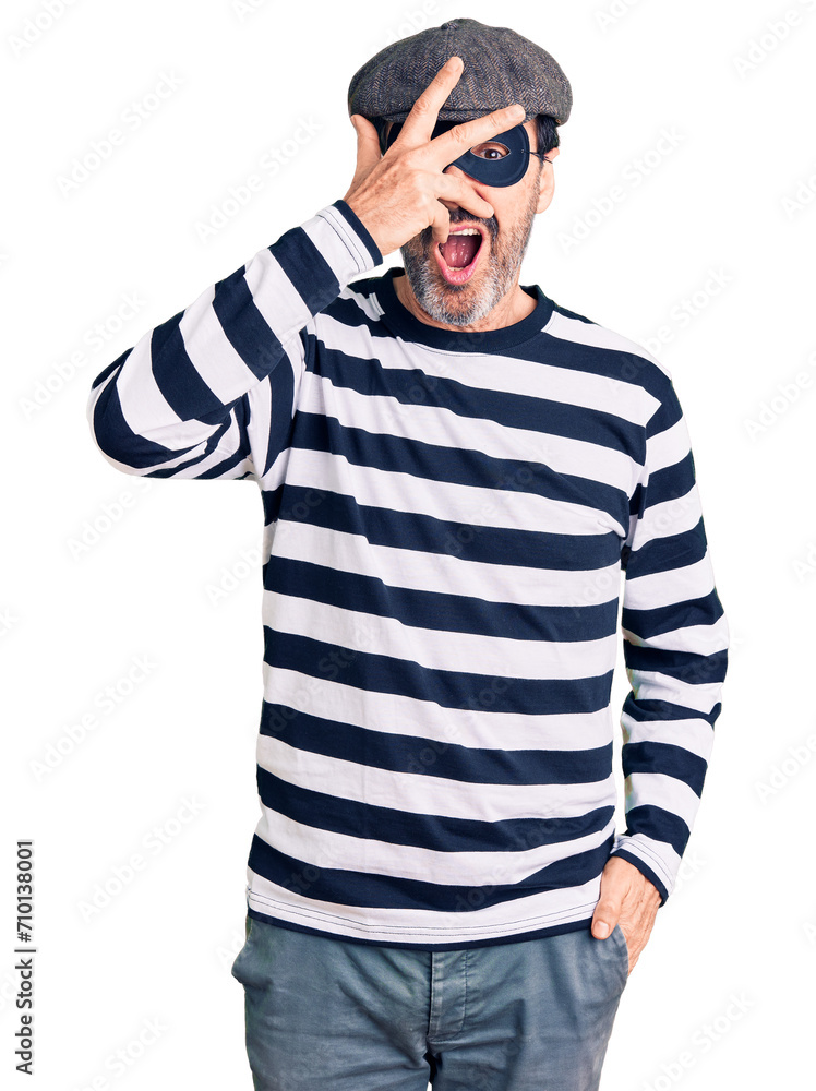 Middle age handsome man wearing burglar mask peeking in shock covering face and eyes with hand, looking through fingers with embarrassed expression. Middle age handsome man wearing burglar mask peeking in shock covering face and eyes with hand, looking through fingers with embarrassed expression.
