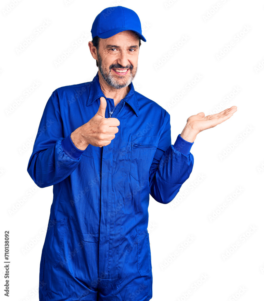 Middle age handsome man wearing mechanic uniform showing palm hand and doing ok gesture with thumbs up, smiling happy and cheerful