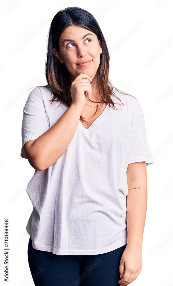 Young beautiful brunette woman wearing casual t-shirt with hand on chin thinking about question, pensive expression. smiling with thoughtful face. doubt concept. Young beautiful brunette woman wearing casual t-shirt with hand on chin thinking about question, pensive expression. smiling with thoughtful face. doubt concept.
