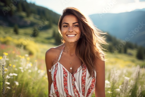 A radiant woman with a captivating smile, wearing a striped romper with a cinching waist belt, standing in a sunlit meadow filled with wildflowers, with a picturesque mountain range in the background photo