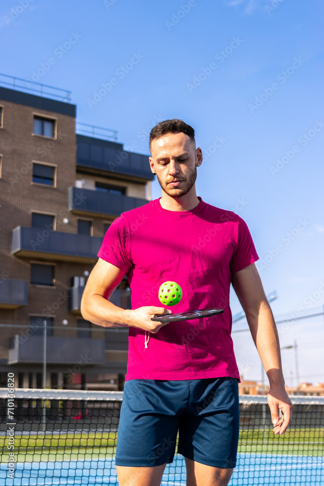 Portrait of a young man playing with a ball and a pickleball racket.