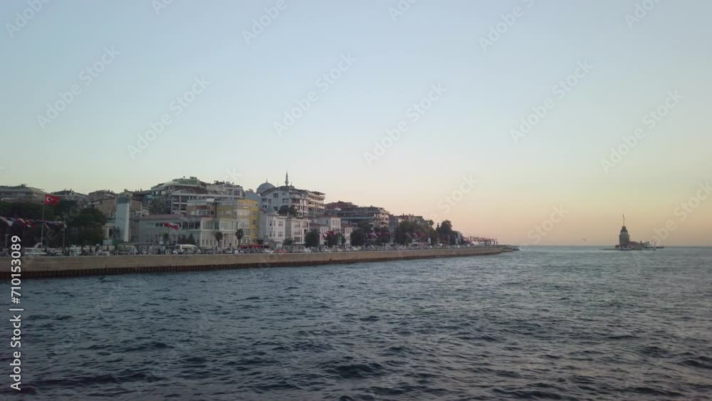Evening, cinematic slow-mo, the view of uskudar and the adjacent Maiden's Tower (Kiz Kulesi) from a ferry sailing along the Istanbul Bosphorus. Golden hour. Traffic is visible on the roads. Evening, cinematic slow-mo, the view of uskudar and the adjacent Maiden's Tower (Kiz Kulesi) from a ferry sailing along the Istanbul Bosphorus. Golden hour. Traffic is visible on the roads.