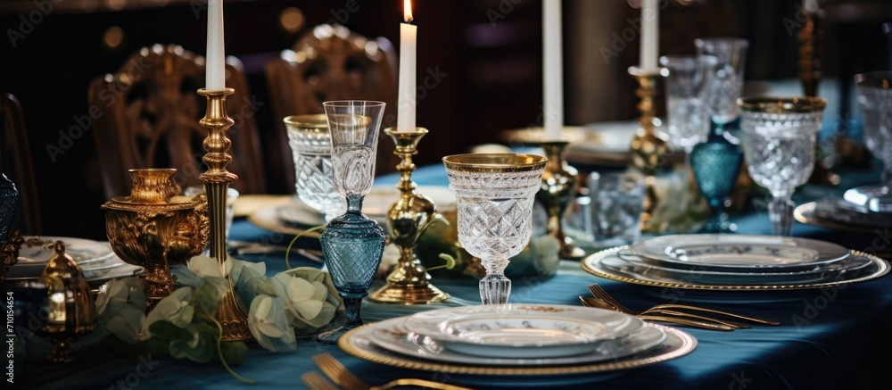 Elegant table with gold-rimmed tableware, candlesticks, patterned cutlery, embossed glasses, and blue velvet tablecloth.