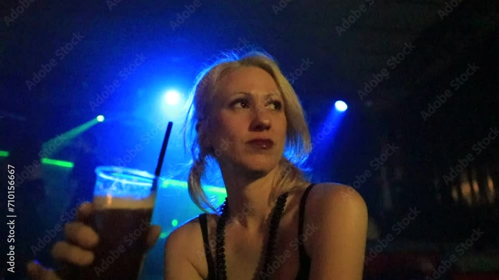 beautiful girl consuming cocktail in a dimly lit dance club illuminated by blue-green laser beams. scene in nighttime entertainment lifestyle with the person consuming the beverage in slow motion. beautiful girl consuming cocktail in a dimly lit dance club illuminated by blue-green laser beams. scene in nighttime entertainment lifestyle with the person consuming the beverage in slow motion.