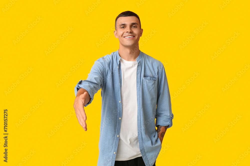 Handsome young man extending hand for handshake on yellow background - obrazy, fototapety, plakaty 