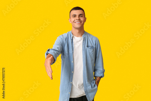 Handsome young man extending hand for handshake on yellow background photo