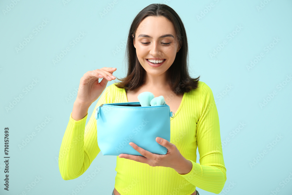 Beautiful young woman with cosmetic bag full of makeup products on blue background Beautiful young woman with cosmetic bag full of makeup products on blue background
