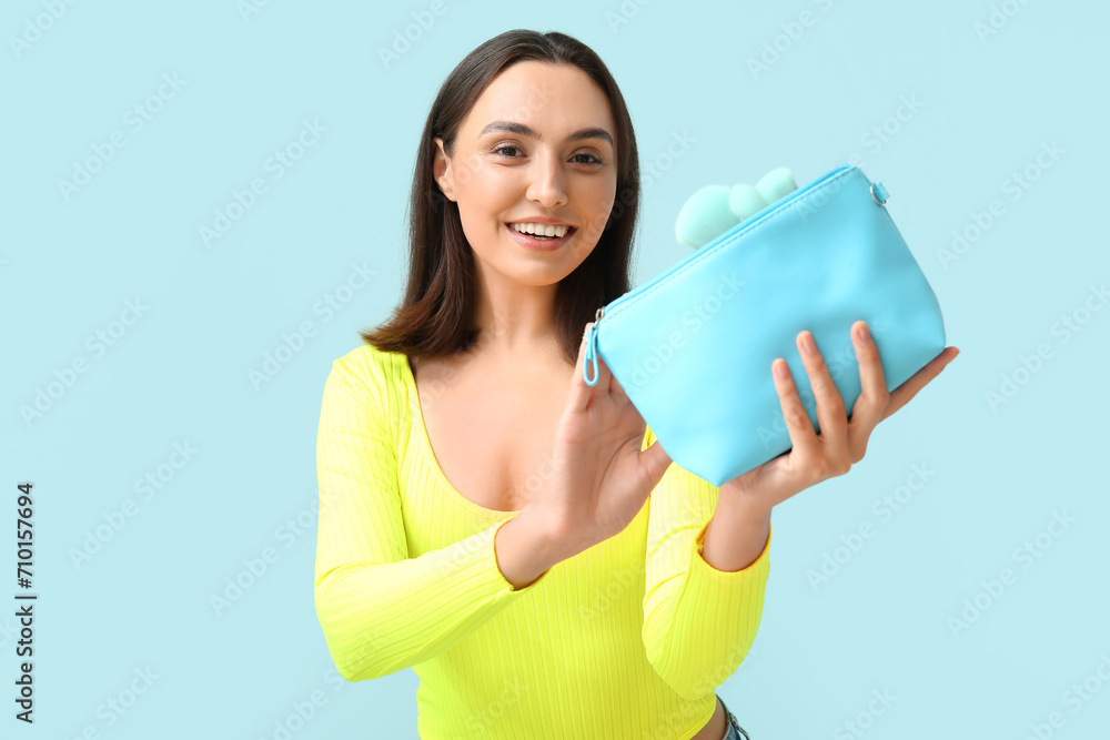 Beautiful young woman with cosmetic bag full of makeup products on blue background Beautiful young woman with cosmetic bag full of makeup products on blue background
