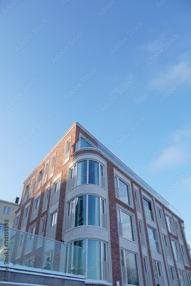 Obraz premium Looking up to red, pink brick new modern building towards light blue sky in Kalamaja. Tallinn, Estonia, Europe. January 2024.