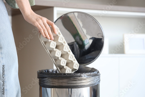 Woman throwing empty egg box into trash bin in kitchen, closeup photo