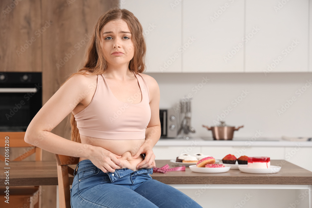Sad young woman in tight jeans sitting at home. Weight gain concept