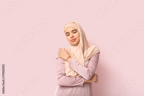 Beautiful young Muslim woman in hijab on pink background