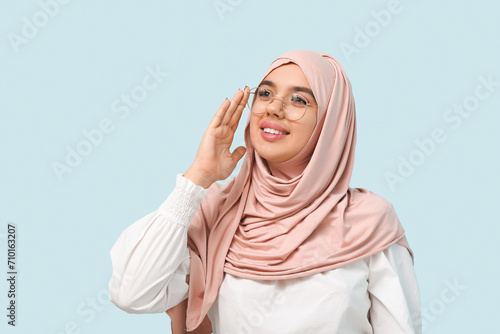 Beautiful young Muslim woman in hijab and eyeglasses on blue background © Pixel-Shot