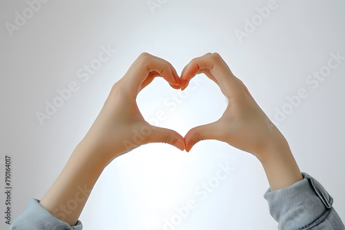 Person making heart shape with hands against plain white background. Clear focal point