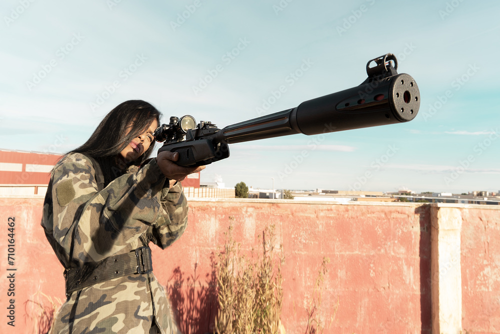 Fototapeta premium Black African women in military uniform aim at a rifle scope, selectively focusing. Military action, a man shoots with a rifle close-up. A dark-skinned woman hunts with a gun