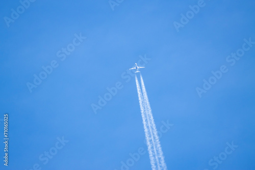 An airplane crossing the blue sky leaving a white trail of steam.