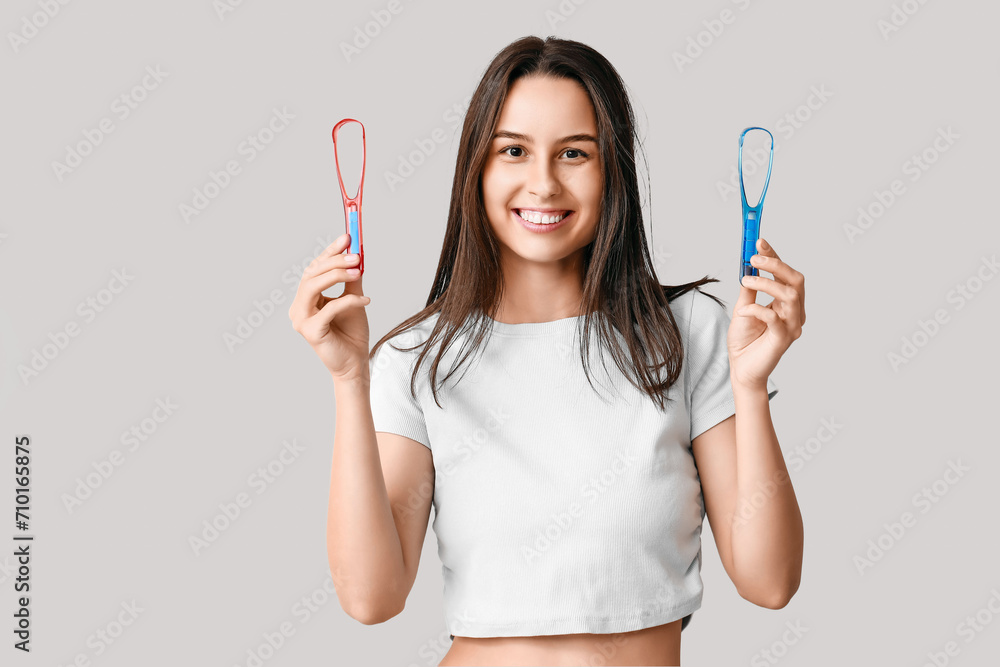 Beautiful young woman with tongue scrapers on grey background Beautiful young woman with tongue scrapers on grey background
