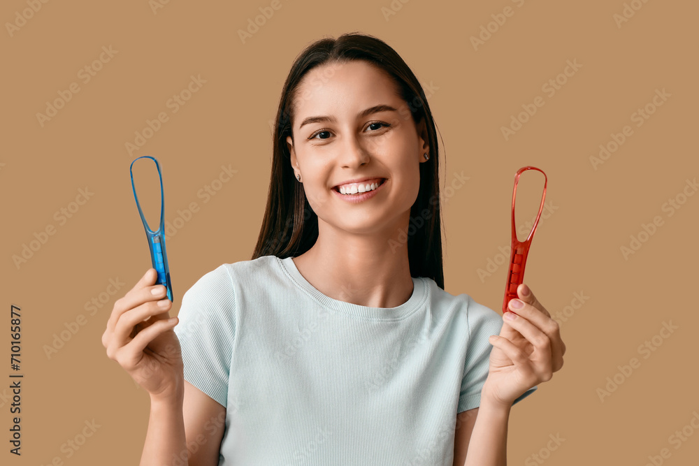Beautiful young woman with tongue scrapers on brown background Beautiful young woman with tongue scrapers on brown background