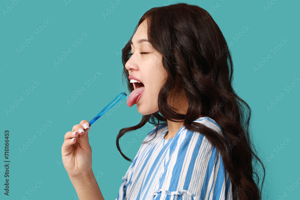 Beautiful young Asian woman with tongue scraper on blue background Beautiful young Asian woman with tongue scraper on blue background