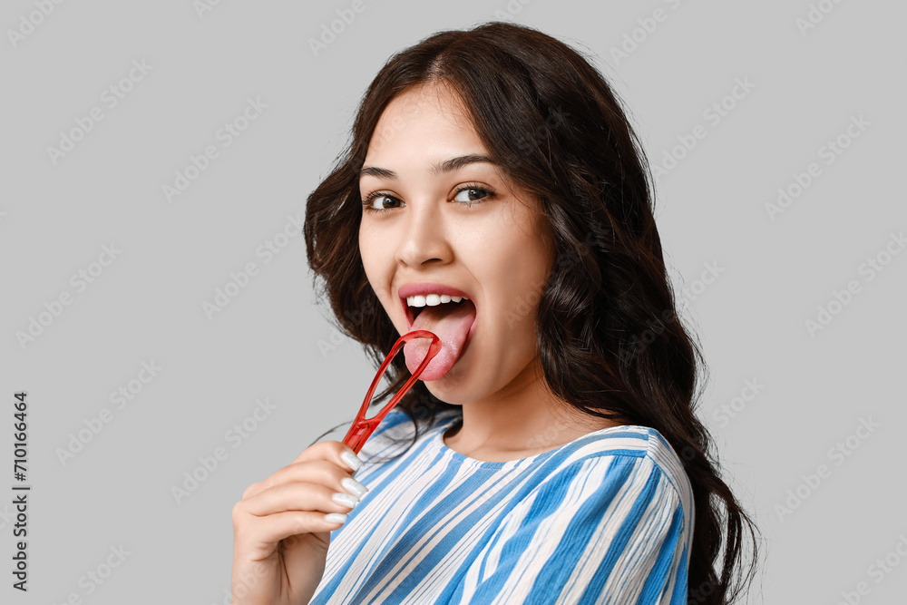 Young Asian woman with tongue scraper on grey background - obrazy, fototapety, plakaty 