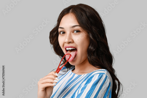 Young Asian woman with tongue scraper on grey background