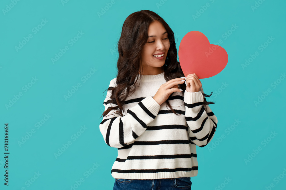 Beautiful young Asian woman with red paper heart on blue background. Valentine's Day celebration Beautiful young Asian woman with red paper heart on blue background. Valentine's Day celebration