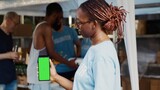Close-up of african american lady vertically grasping mobile device having blank copyspace chromakey template. During charitable food bank black woman volunteer holds cellphone with green screen.