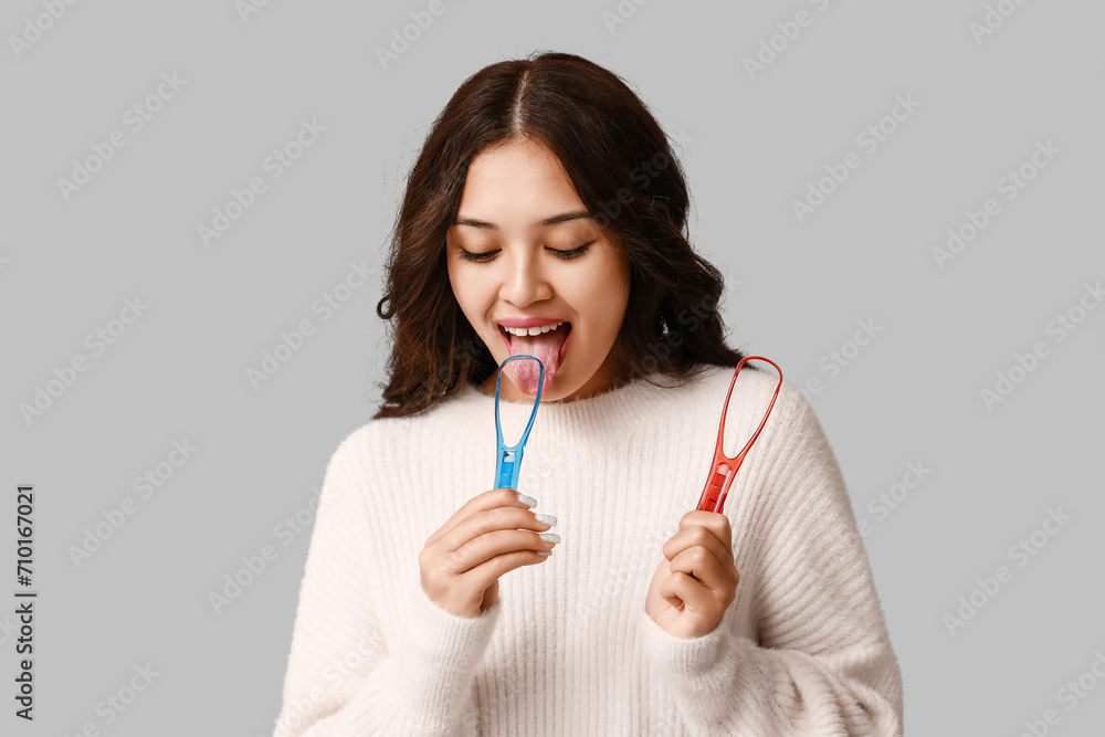 Young Asian woman with tongue scrapers on grey background Young Asian woman with tongue scrapers on grey background