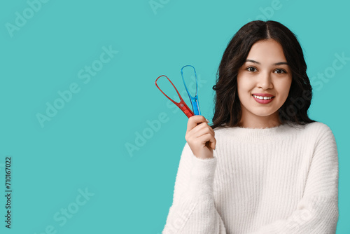 Happy young Asian woman with tongue scrapers on blue background