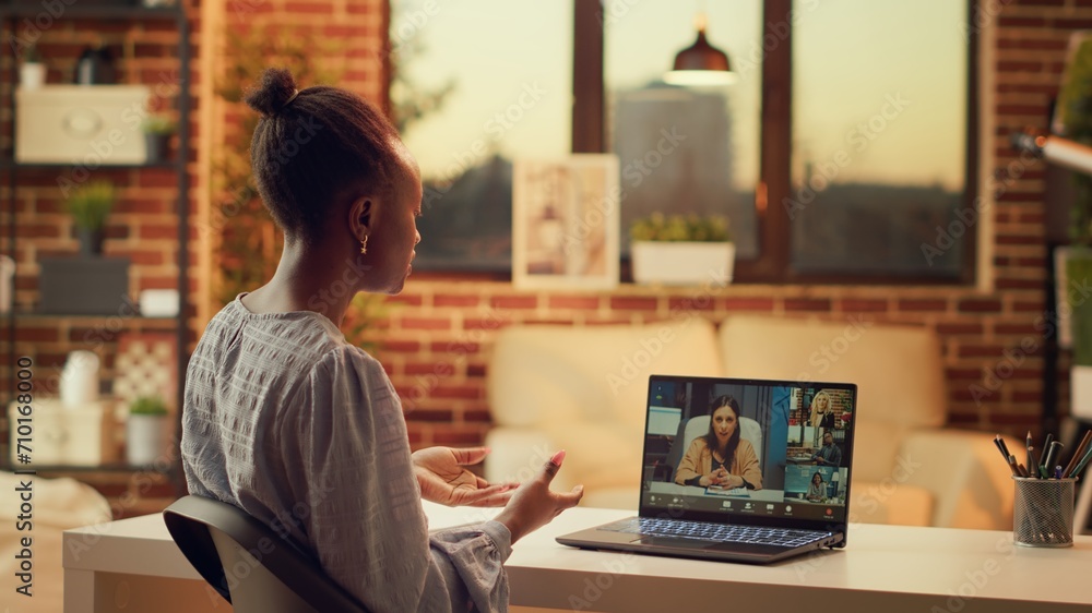 Worker chatting with clients on videocall, talking about price list and services to build online career in freelancing job. Woman using teleconference remote call at home, sunset light.