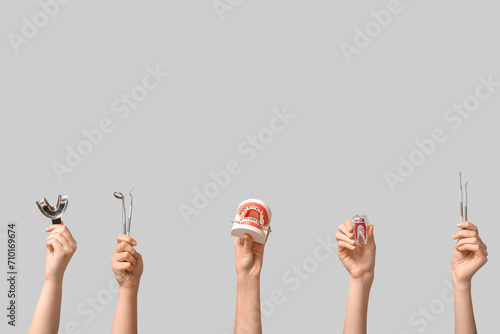 Female hands with jaw model, plastic tooth and dental tools on grey background