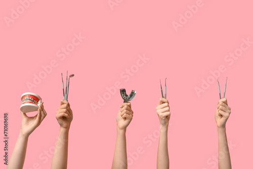 Female hands with dental tools and jaw model on pink background