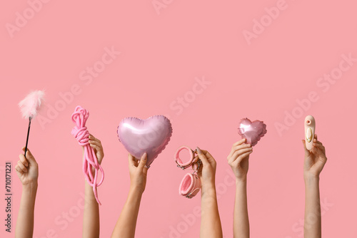 Many female hands with heart shaped balloons and sex toys on pink background. Valentine's Day celebration photo