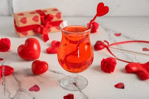 Glass of tasty cocktail with hearts and roses on light table, closeup. Valentine's Day celebration