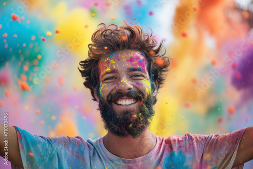 Happy bearded man celebrating Holi festival, portrait of person with paint on face. Smiling guy on colorful powder background. Concept of India, fun, party, color, people, Indian