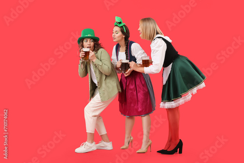 Portrait of women with beer celebrating St. Patrick's Day on red background