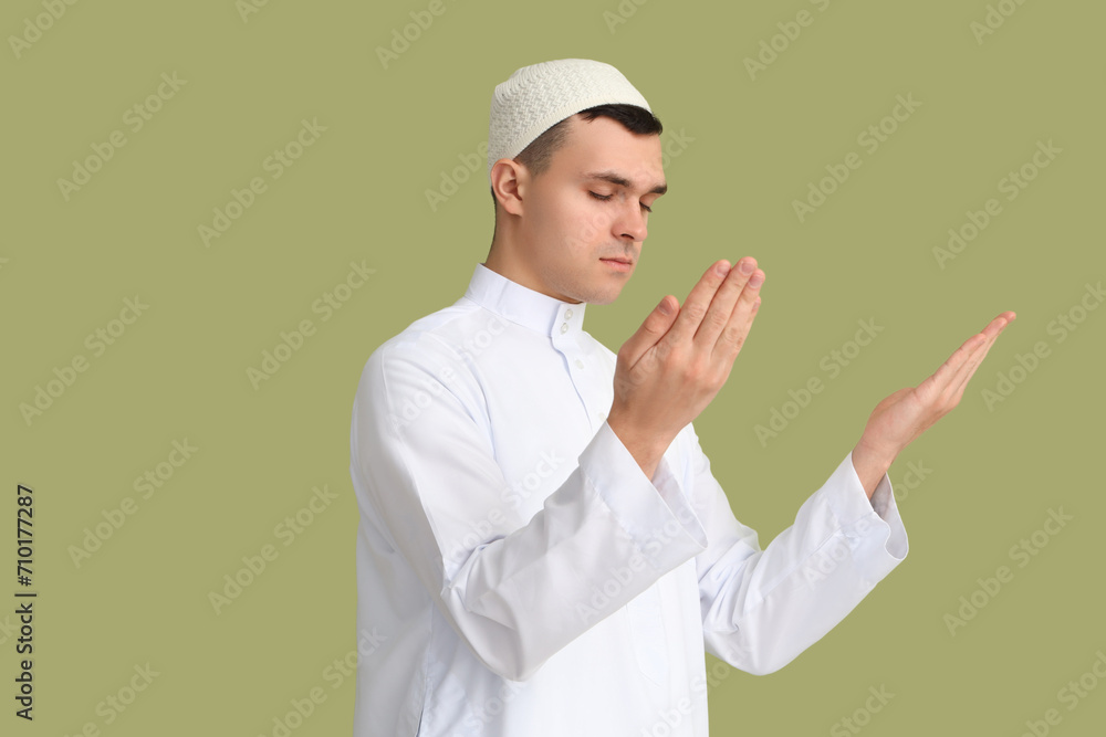 Young Muslim man praying on green background. Ramadan celebration