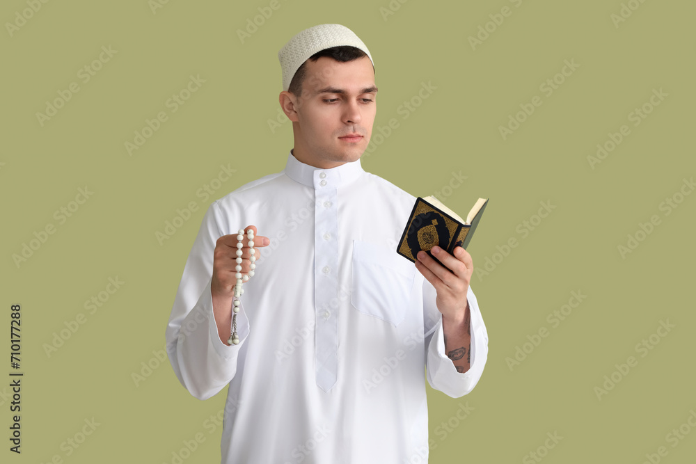 Young Muslim man with praying beads and Koran on green background. Ramadan celebration Young Muslim man with praying beads and Koran on green background. Ramadan celebration