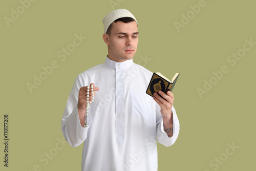 Young Muslim man with praying beads and Koran on green background. Ramadan celebration
